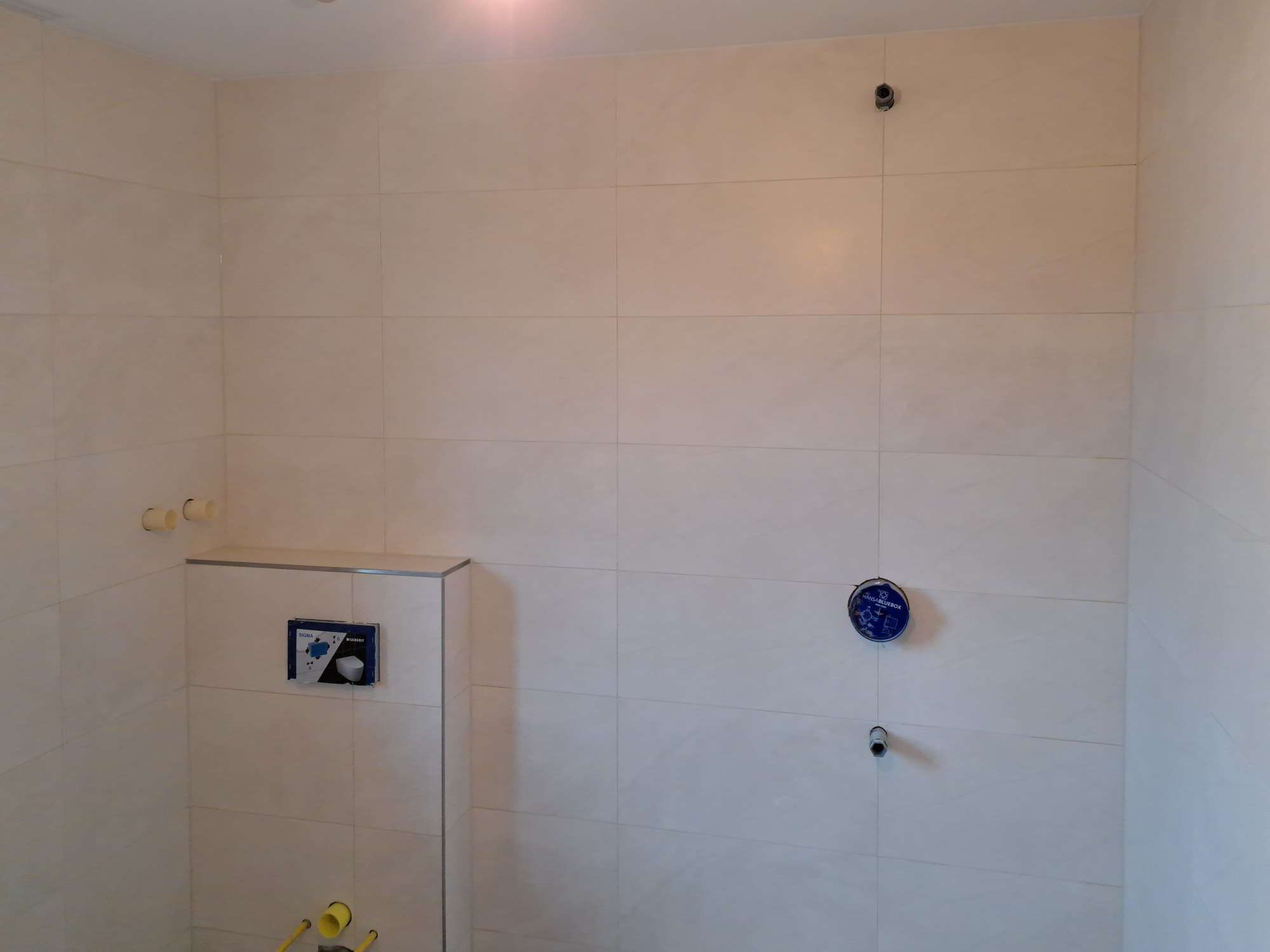 Łazienka w jasnych płytkach układanych poziomo, z obudowanym stelażem WC i otworami pod baterię