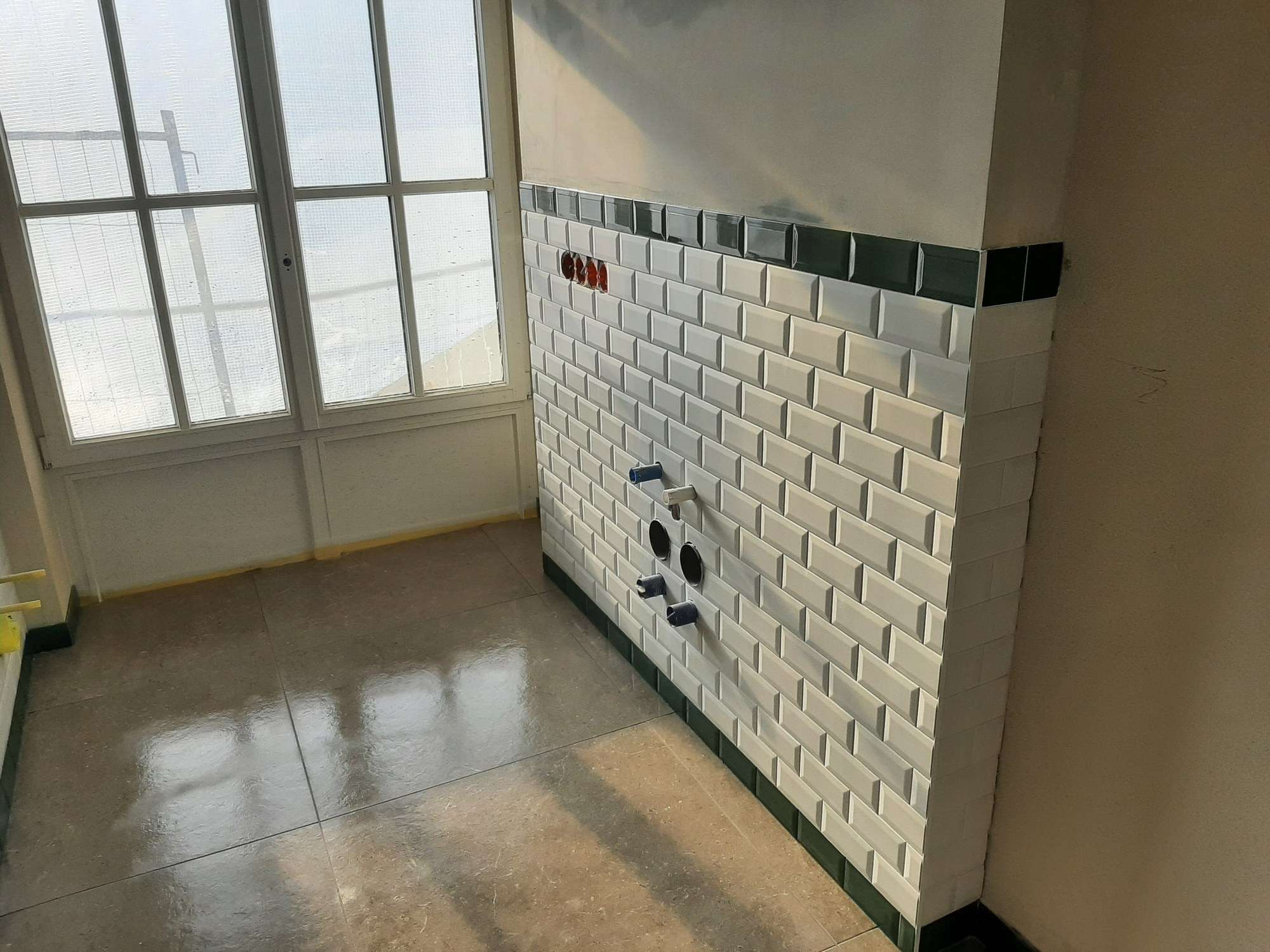 Ściana z białych płytek metro z ciemnozielonym pasem u góry i u dołu, w płytkach otwory pod armaturę